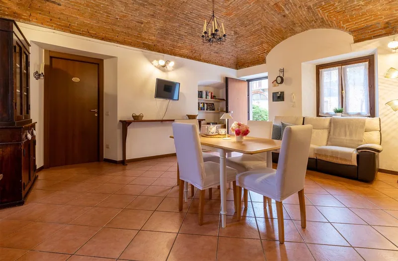 Soggiorno de Il Monastero con volta a mattoni a vista, lampadario in ferro, tavolo da pranzo bianco e pavimento in cotto